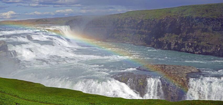 Breiter Wasserfall überspannt von einem Regenbogen.