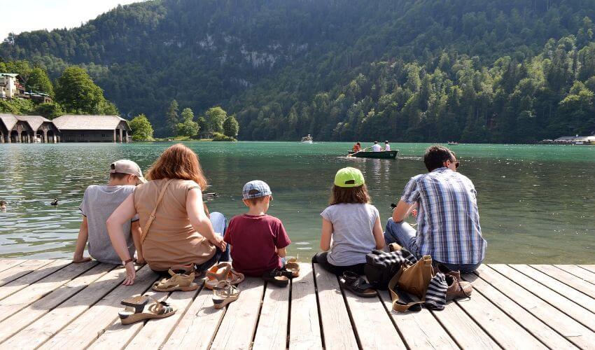 Eine Familie mit 3 Kindern sitzt am Steg eines Sees.
