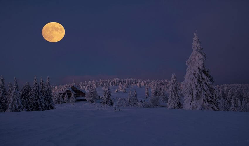 Vollmond über eine beschneite Winterlandschaft.