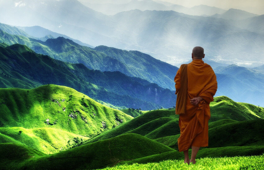 Ein Mönch steht auf einem Hügel und blickt über einen grün bewachsenen Berg.