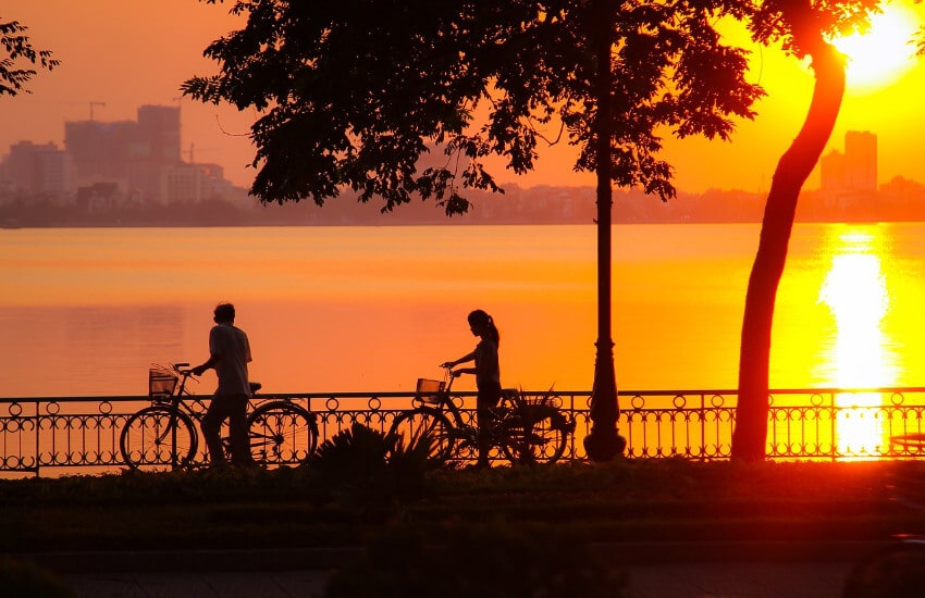 Zwei Radfahrer schieben Ihr Rad entlang eines Sees bei Sonnenuntergang.