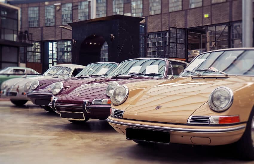 Ein gelber, zwei weinrote und ein grauer Porsche nebeneinander in einem Museum.