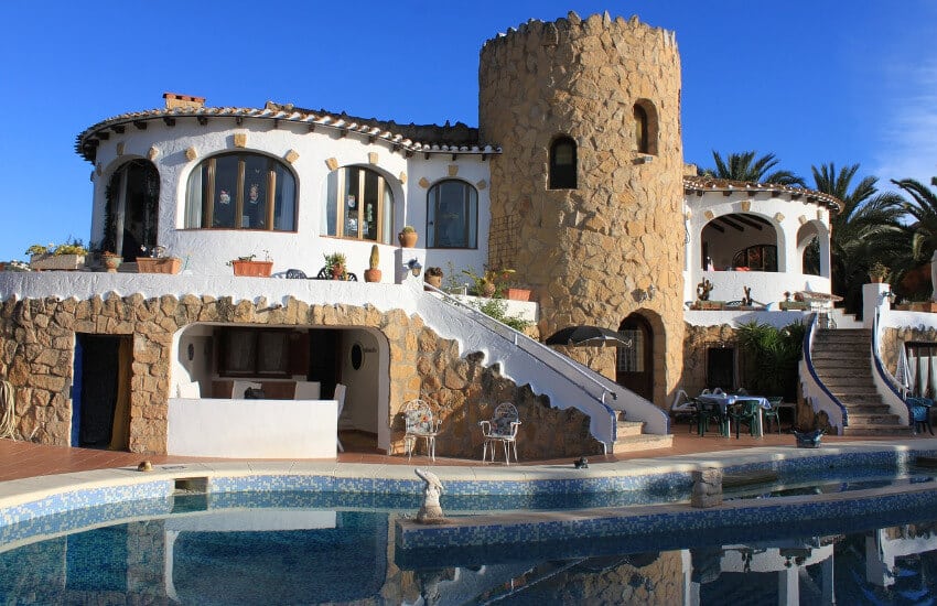 Ein weißes Ferienhaus teilweise mit Steinoptik und einem Pool davor.